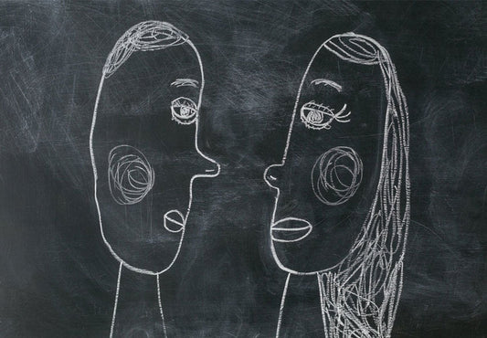 Two chalk-drawn face profiles facing each other on a dark chalkboard, representing the contrasting thinking styles of mom brain and dad brain