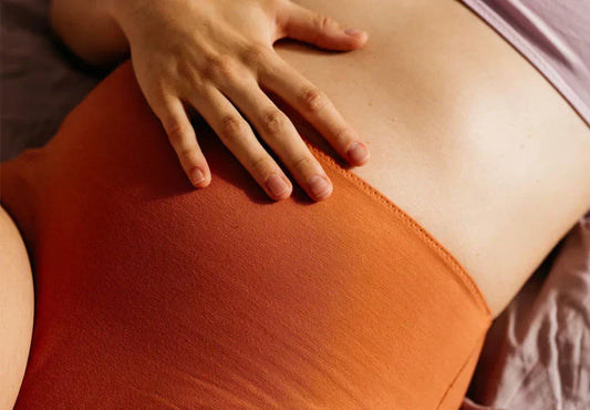 Close-up of hands resting gently on a pregnant belly in a rust-coloured crop top, representing awareness of abdominal changes during pregnancy
