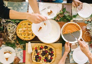 Overhead view of a holiday table spread with pies and food being shared by hands, representing gratitude and family connection