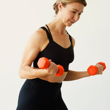 A woman in a black top curling an orange hand weight